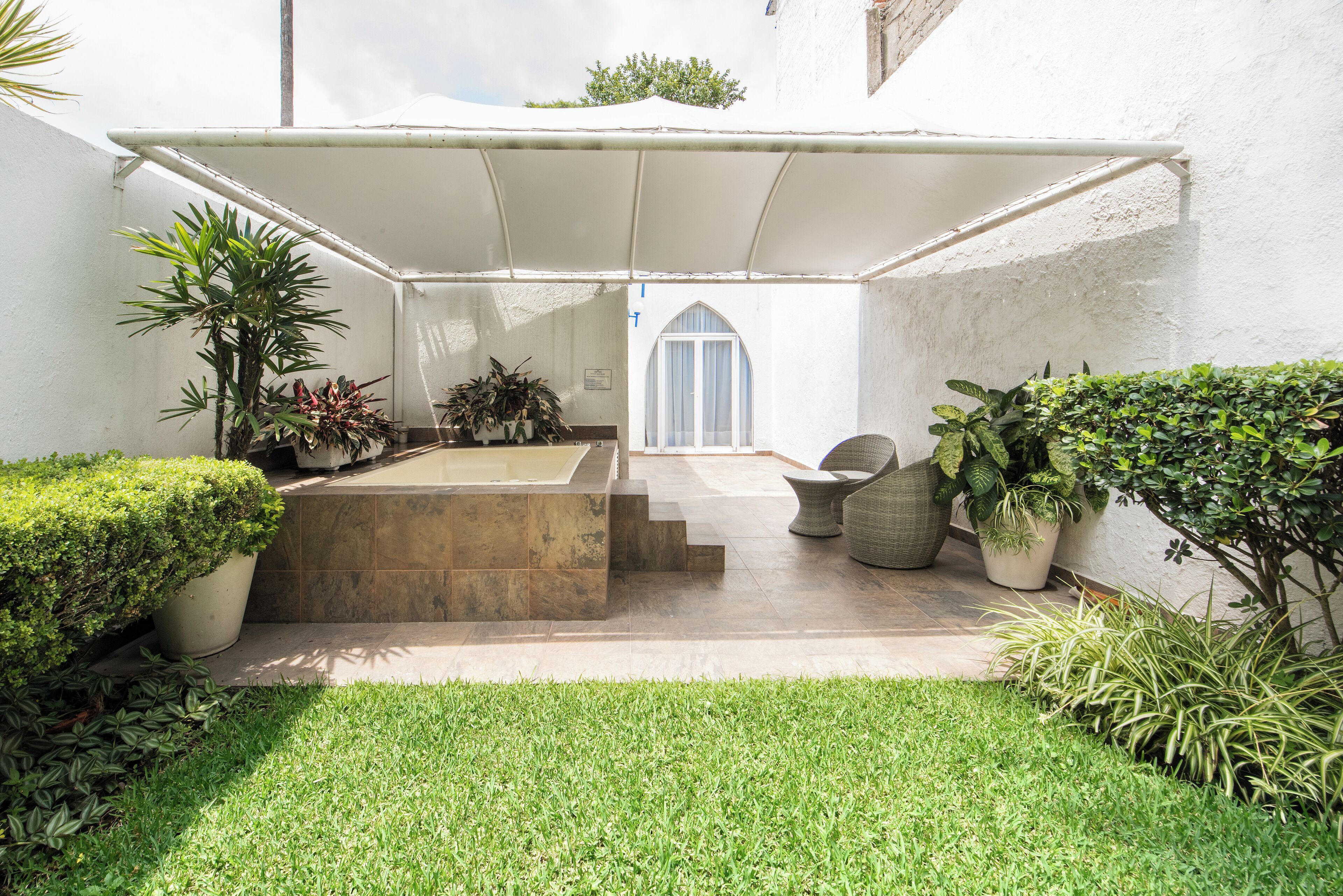 Un patio cubierto con un banco de piedra, plantas en macetas y vista de un edificio al fondo.