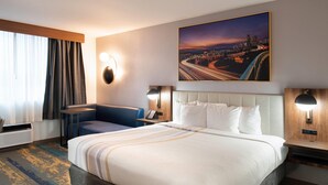 A hotel room with a large bed, a desk, a chair, a cityscape painting, and a night sky view. - La Quinta Inn & Suites by Wyndham Seattle Sea-Tac Airport (SeaTac)
