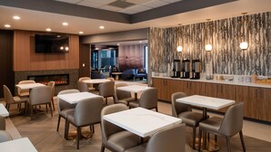 A modern restaurant with multiple tables and chairs, a flat-screen TV mounted on the wall, a fireplace, and a bar area with various amenities. - La Quinta Inn & Suites by Wyndham Seattle Sea-Tac Airport (SeaTac)
