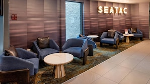 A modern lounge area with seating, a large window, and a sign reading 'SEATAC'. - La Quinta Inn & Suites by Wyndham Seattle Sea-Tac Airport (SeaTac)