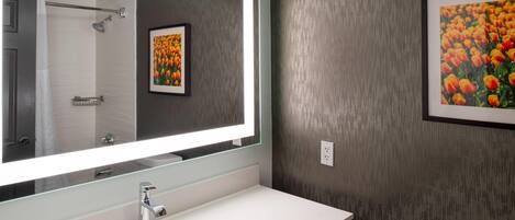 A bathroom with a large mirror, a white sink, a toilet, and a framed picture of flowers on the wall.