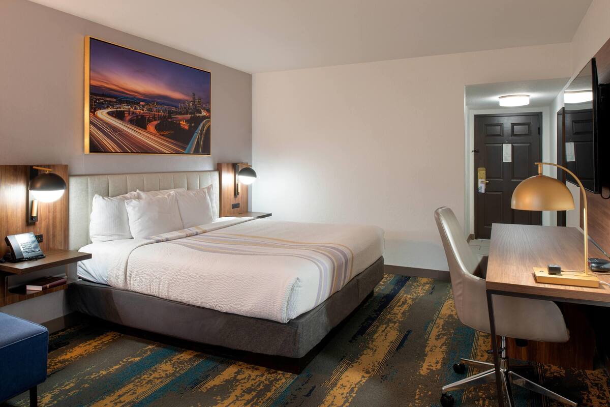 Ein Hotelzimmer mit Bett, Schreibtisch, Stuhl und einem Stadtbild an der Wand.