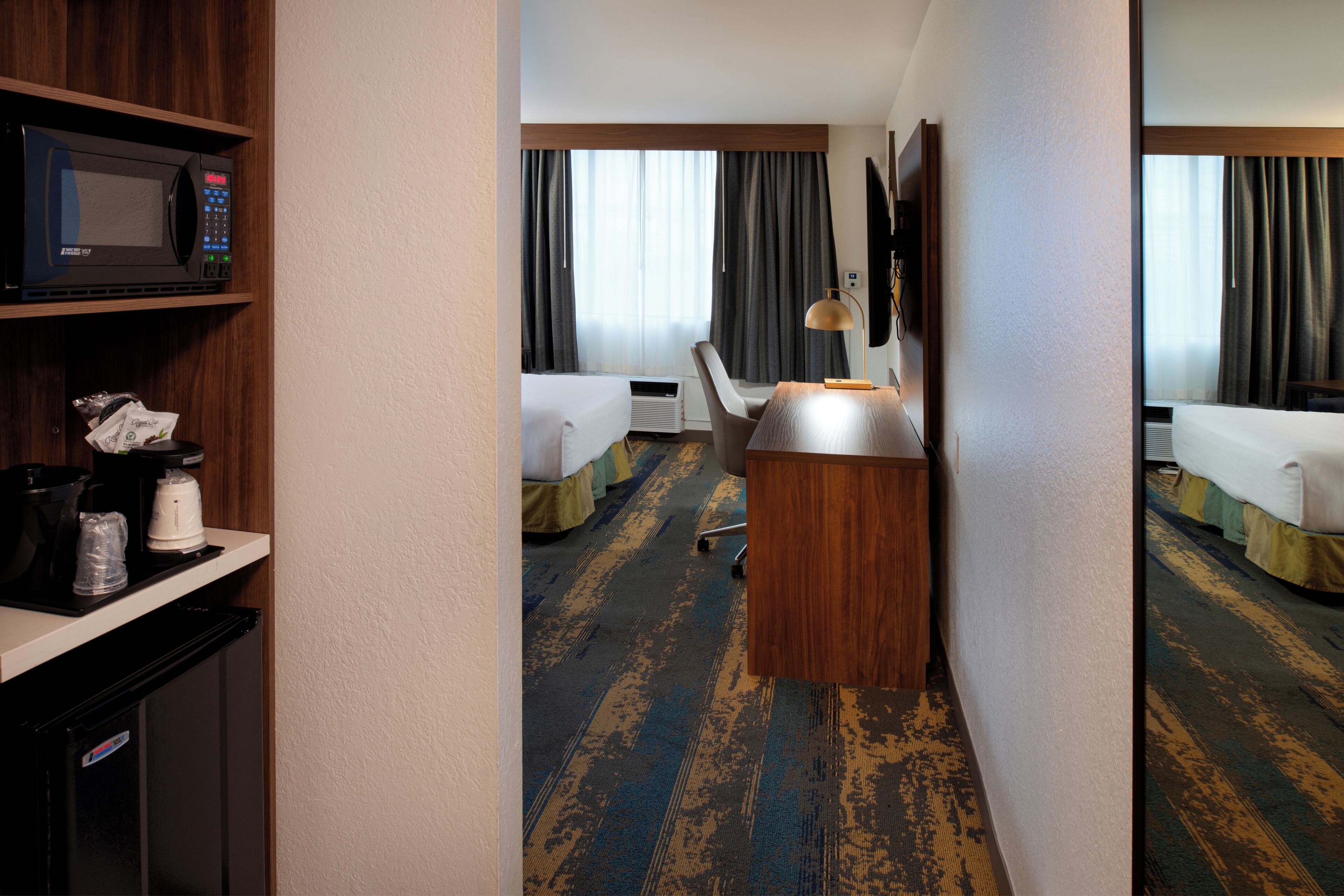 A hotel room with a kitchenette, a bed, a desk, and a TV.