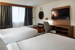 Ein Hotelzimmer mit zwei Betten, einem Schreibtisch, einem Sessel, einem Fernseher und einem Fenster mit Vorhängen.