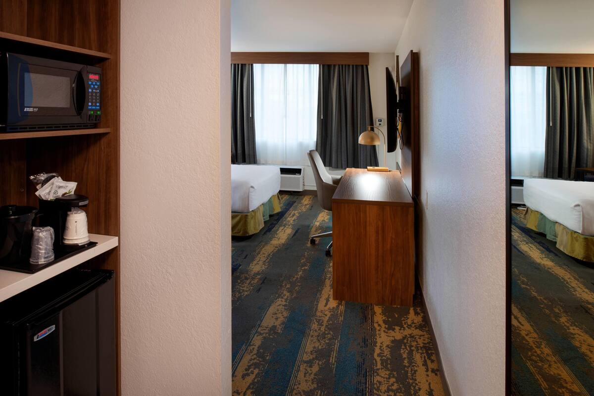 Ein Hotelzimmer mit Mikrowelle, Schreibtisch, Stuhl, Bett und einem großen Fenster mit Vorhängen.