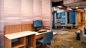 A modern office space with a wooden desk, a computer, and a blue chair. There are two chairs and a small table in the background. - La Quinta Inn & Suites by Wyndham Seattle Sea-Tac Airport (SeaTac)