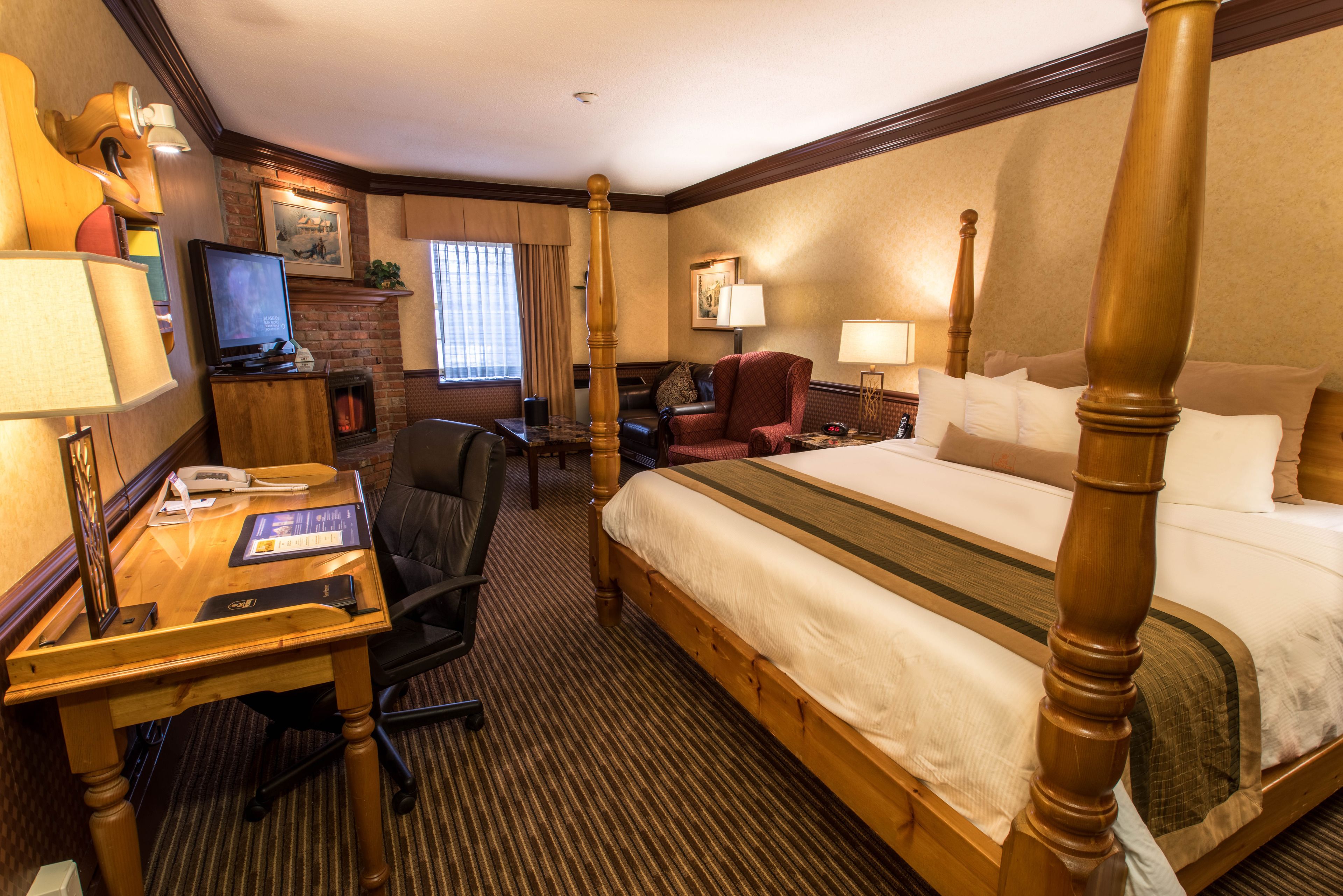 A hotel room with a four-poster bed, a desk with a computer, a television, and a fireplace.