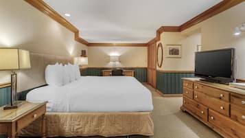 Ein Hotelzimmer mit einem großen Bett, einem Holzschrank, einem Fernseher, einem Schreibtisch, einer Lampe und einem gerahmten Bild an der Wand.
