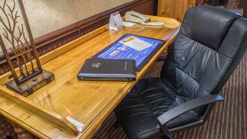 Un mostrador de recepción de madera con una silla de cuero negro, un teléfono, un directorio y una computadora portátil.