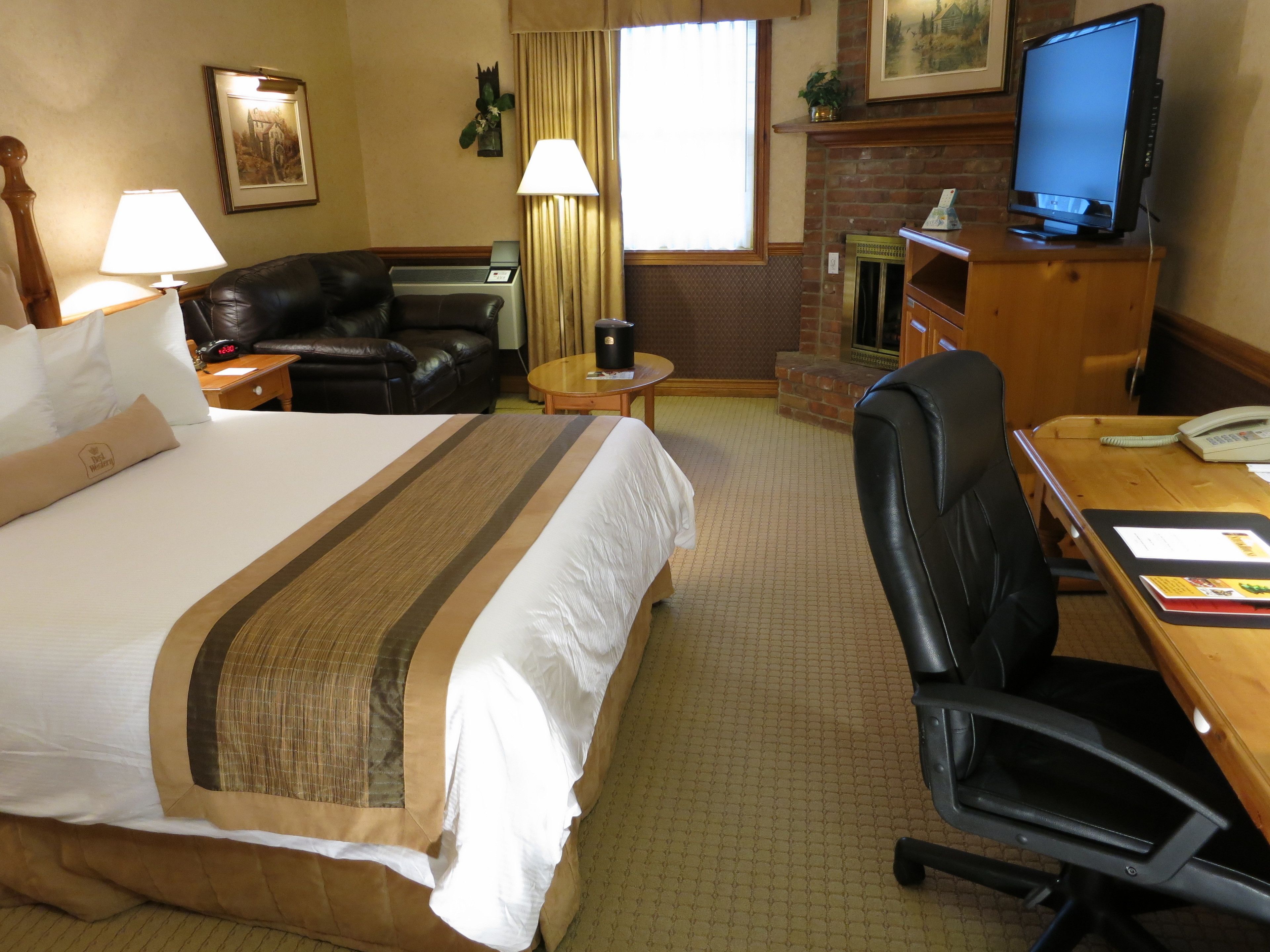 Une chambre d’hôtel avec un grand lit, un canapé en cuir, un bureau avec une chaise, une télévision et une cheminée.