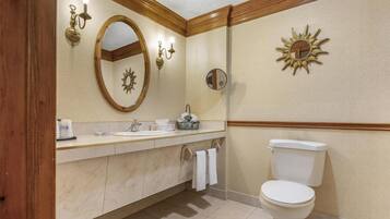 A bathroom with a vanity, sink, mirror, towel rack, toilet, and decorative wall sconces.