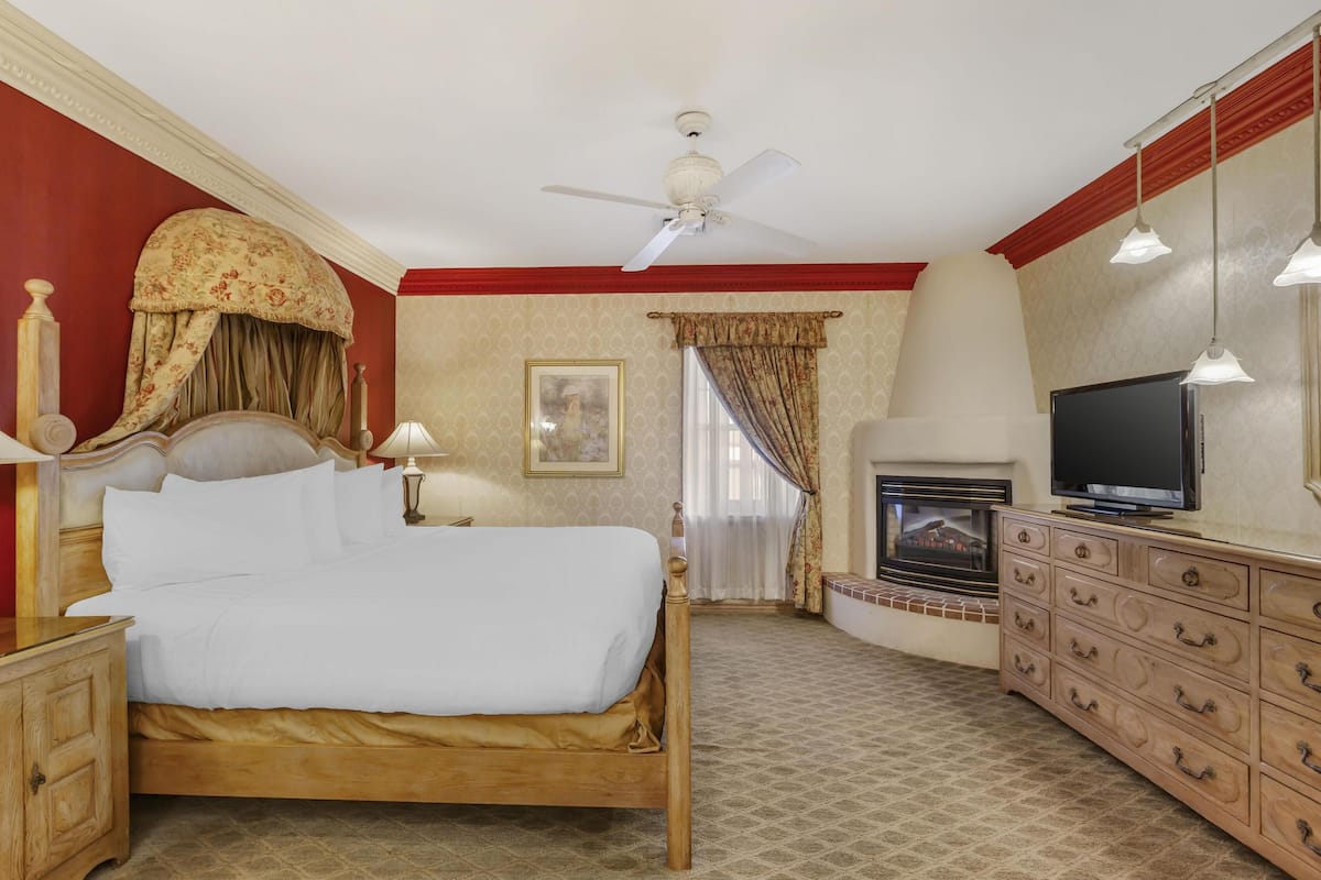 A hotel room with a wooden bed, a television, a dresser, and a ceiling fan.