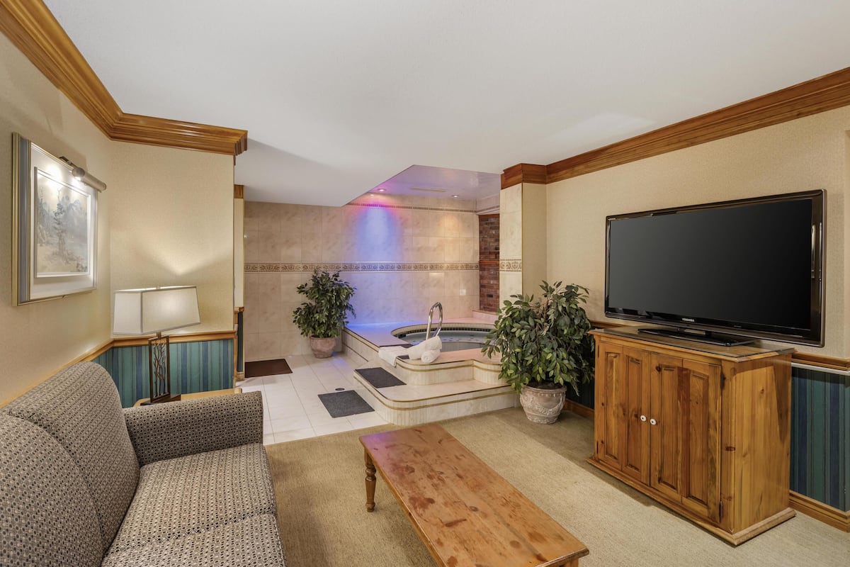 A living room with a sofa, a wooden coffee table, a flat-screen TV, a fireplace, and a hot tub.