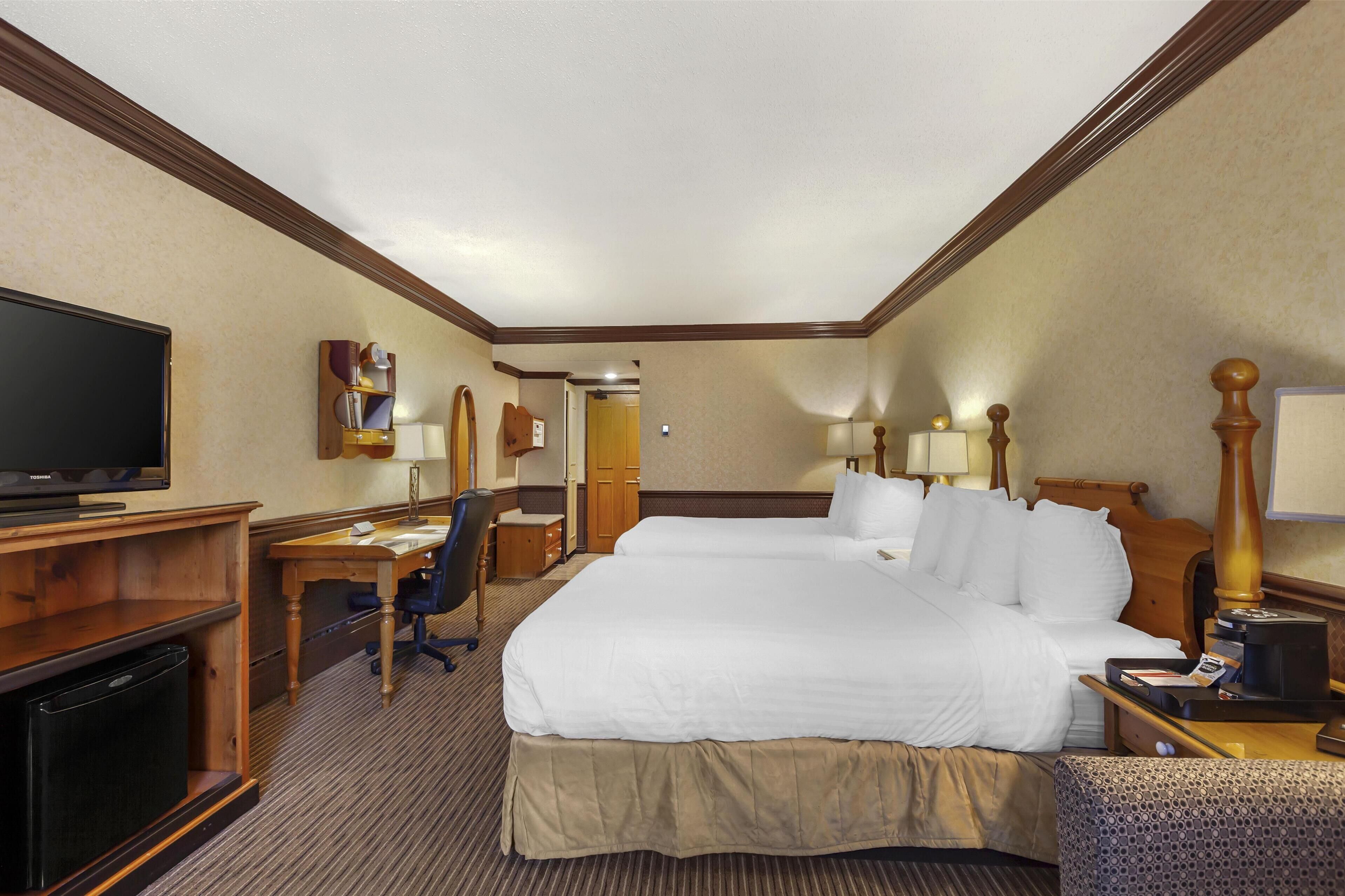 A hotel room with a large bed, a desk with a computer, a television, and a small refrigerator.