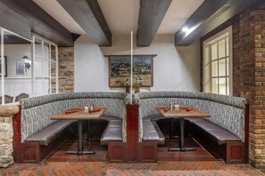 A corner seating area with cushioned benches and tables, a stone wall, a painting, and a wooden ceiling. - Best Western Fireside Inn (Kingston)