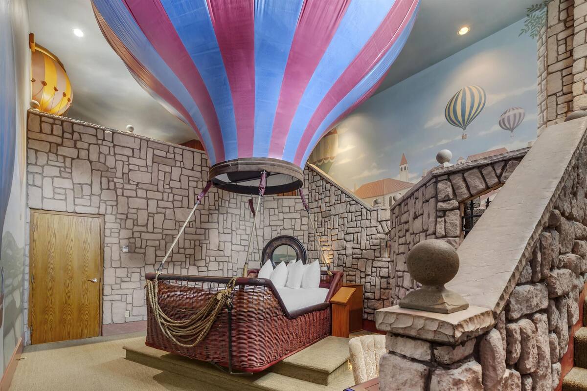 A room with a stone wall, a wicker bed, a stone balustrade, and a mural of hot air balloons.