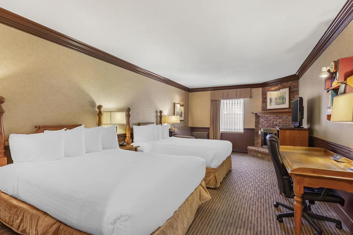 A hotel room with two beds, a desk, a chair, a television, and a fireplace.