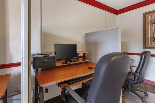 Una habitación de hotel con un escritorio de madera, una silla de oficina negra, un ordenador e impresora.