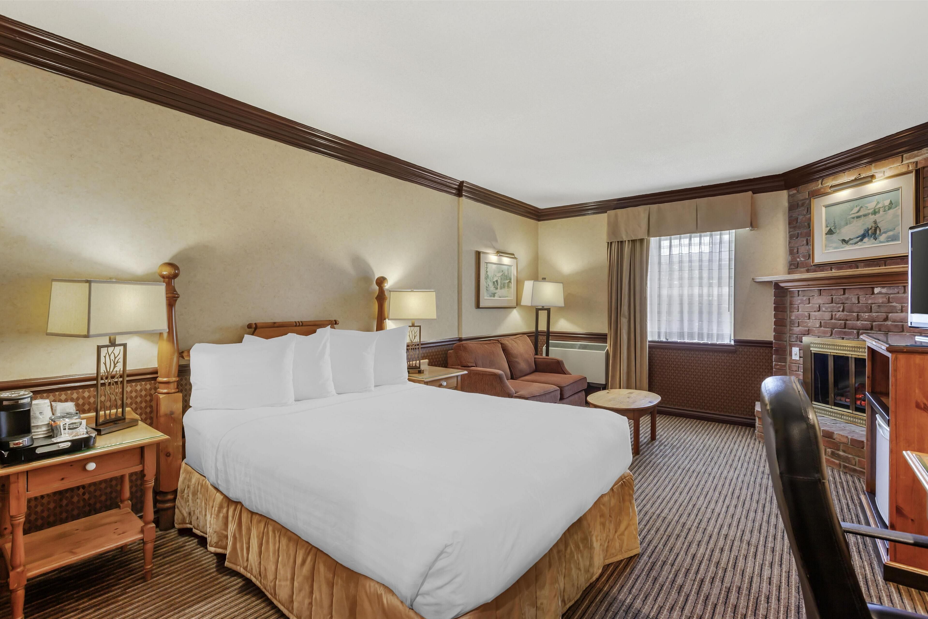 Une chambre d’hôtel avec un grand lit, un bureau avec une lampe, une chaise, une cheminée et une fenêtre avec des rideaux.