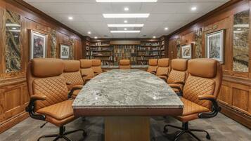 Una sala de conferencias con una mesa de mármol, sillas de cuero, paneles de madera y estanterías.