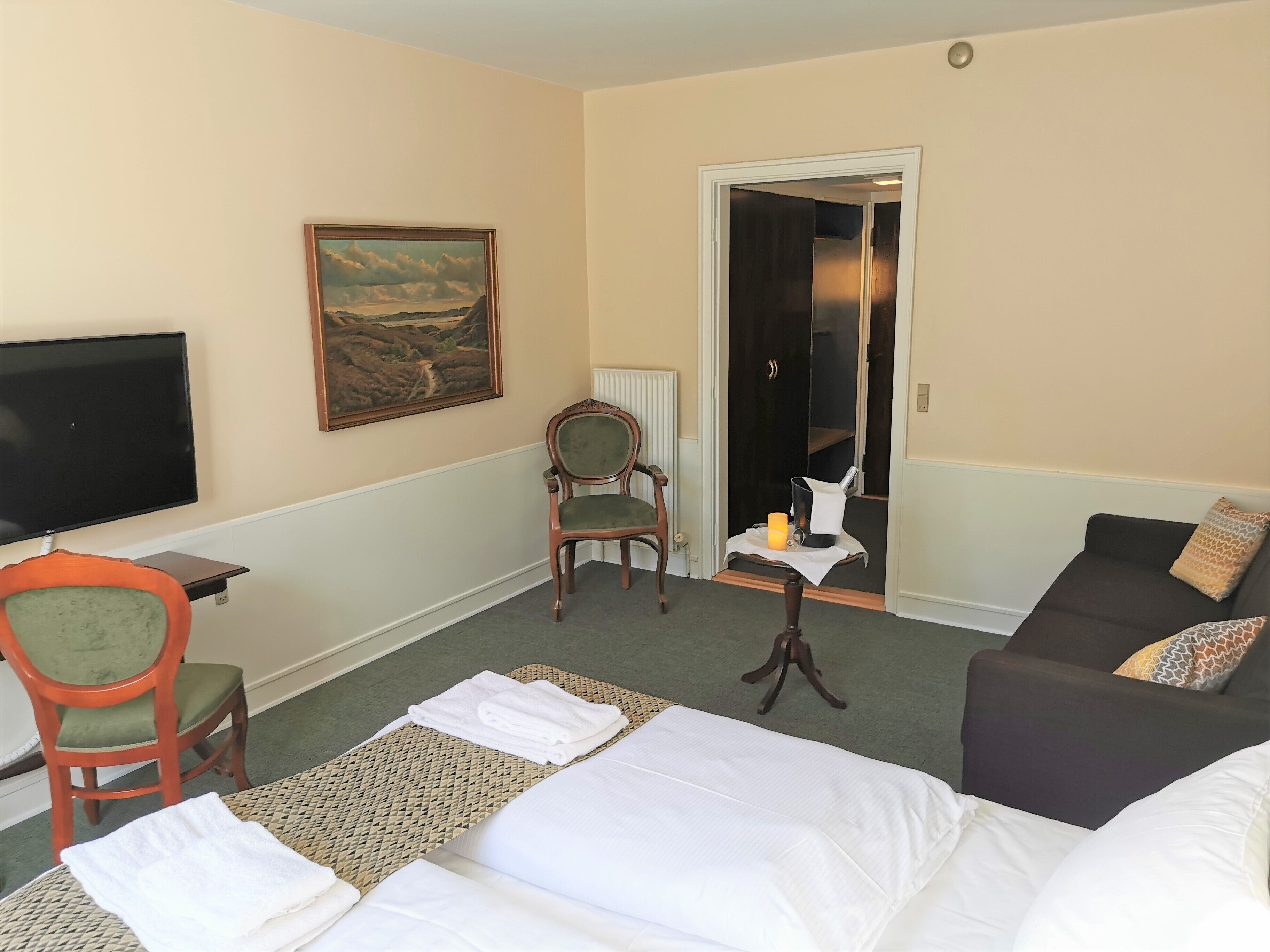 Una habitación de hotel con cama, sillón, sofá, televisor y un cuadro en la pared.
