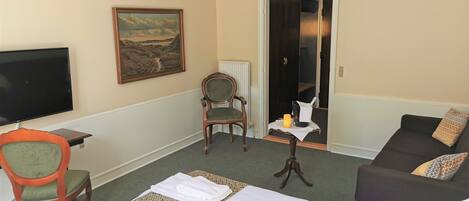 A hotel room with a bed, a chair, a sofa, a television, and a painting on the wall.