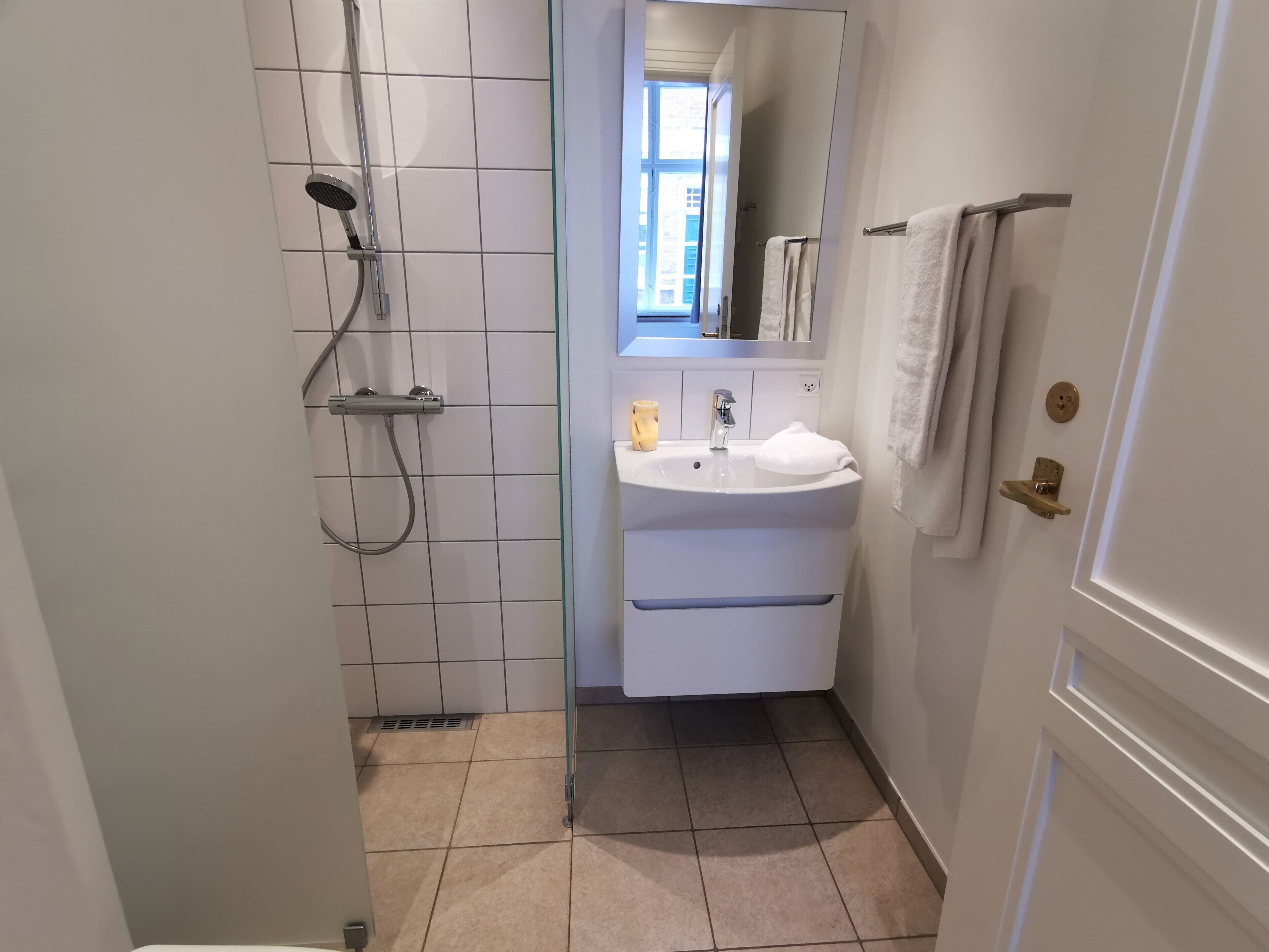 Et lille badeværelse med bruser, vask og spejl.