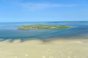 An aerial view of a coastal island with clear blue waters, sandy beaches, and green fields.