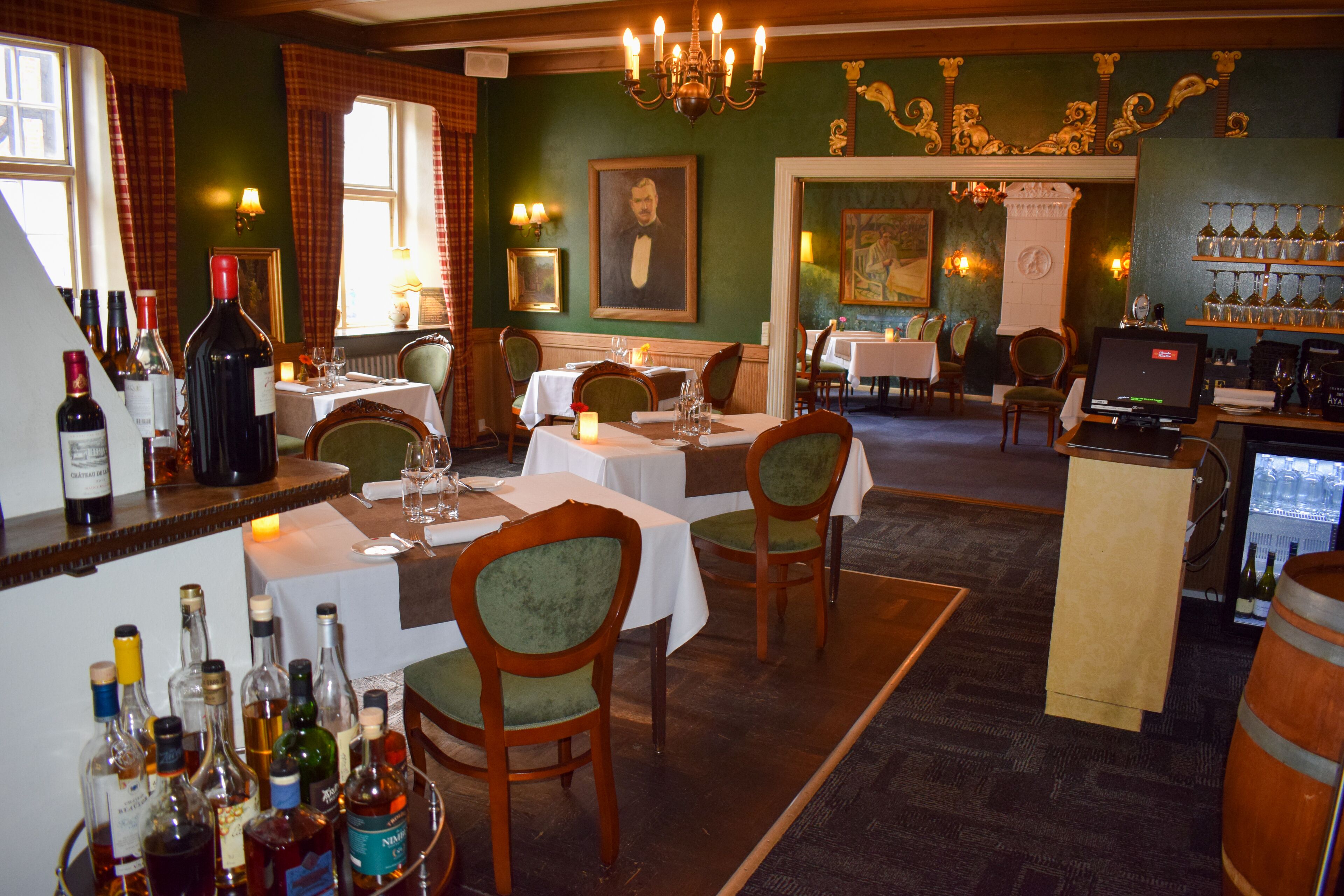 A restaurant with tables set for dining, a bar area with bottles, and a mural on the wall.