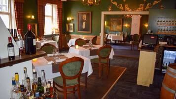 A restaurant with tables set for dining, a bar area with bottles, and a mural on the wall.