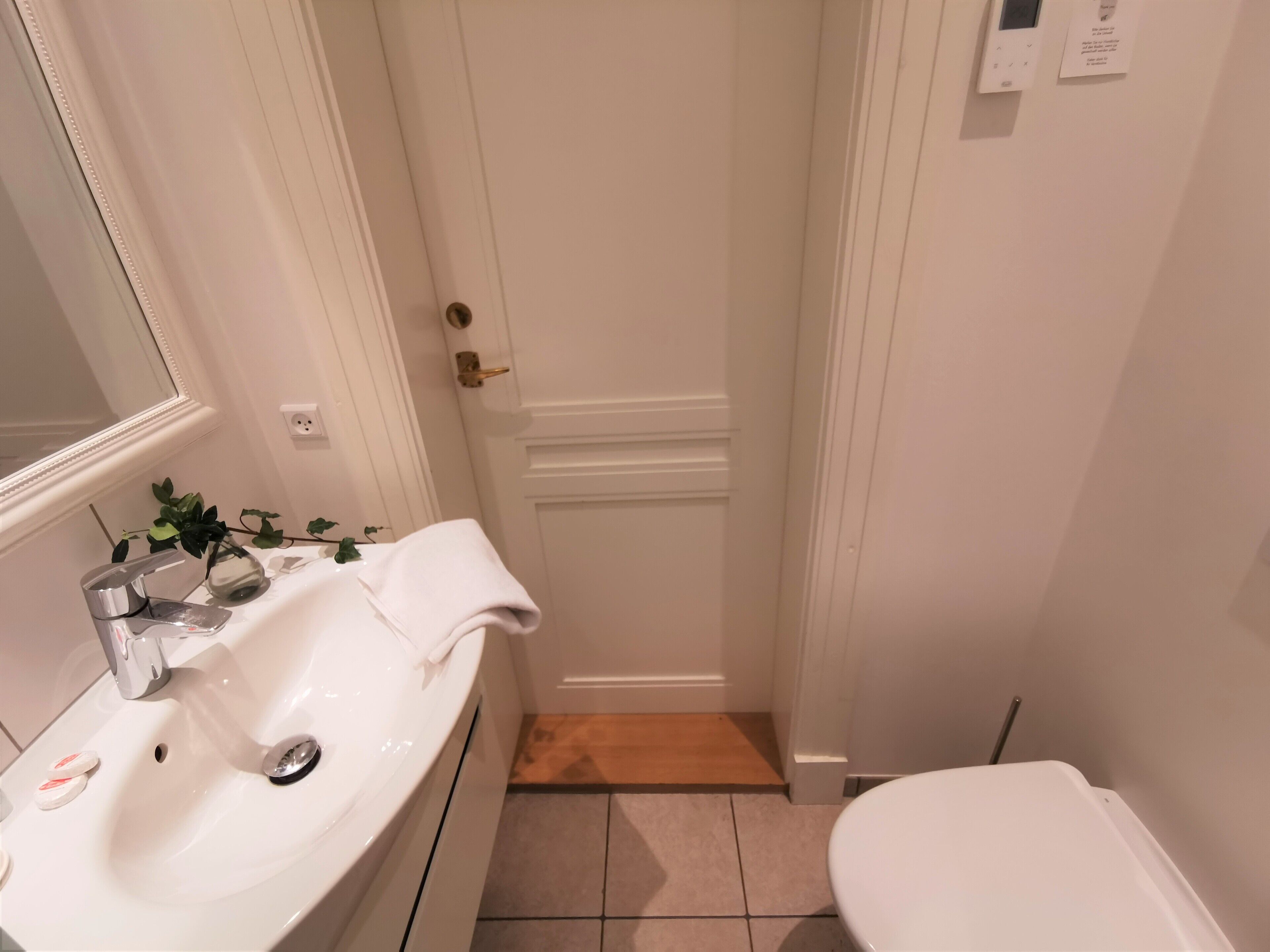 A bathroom with a white sink, a mirror, a toilet, and a door.