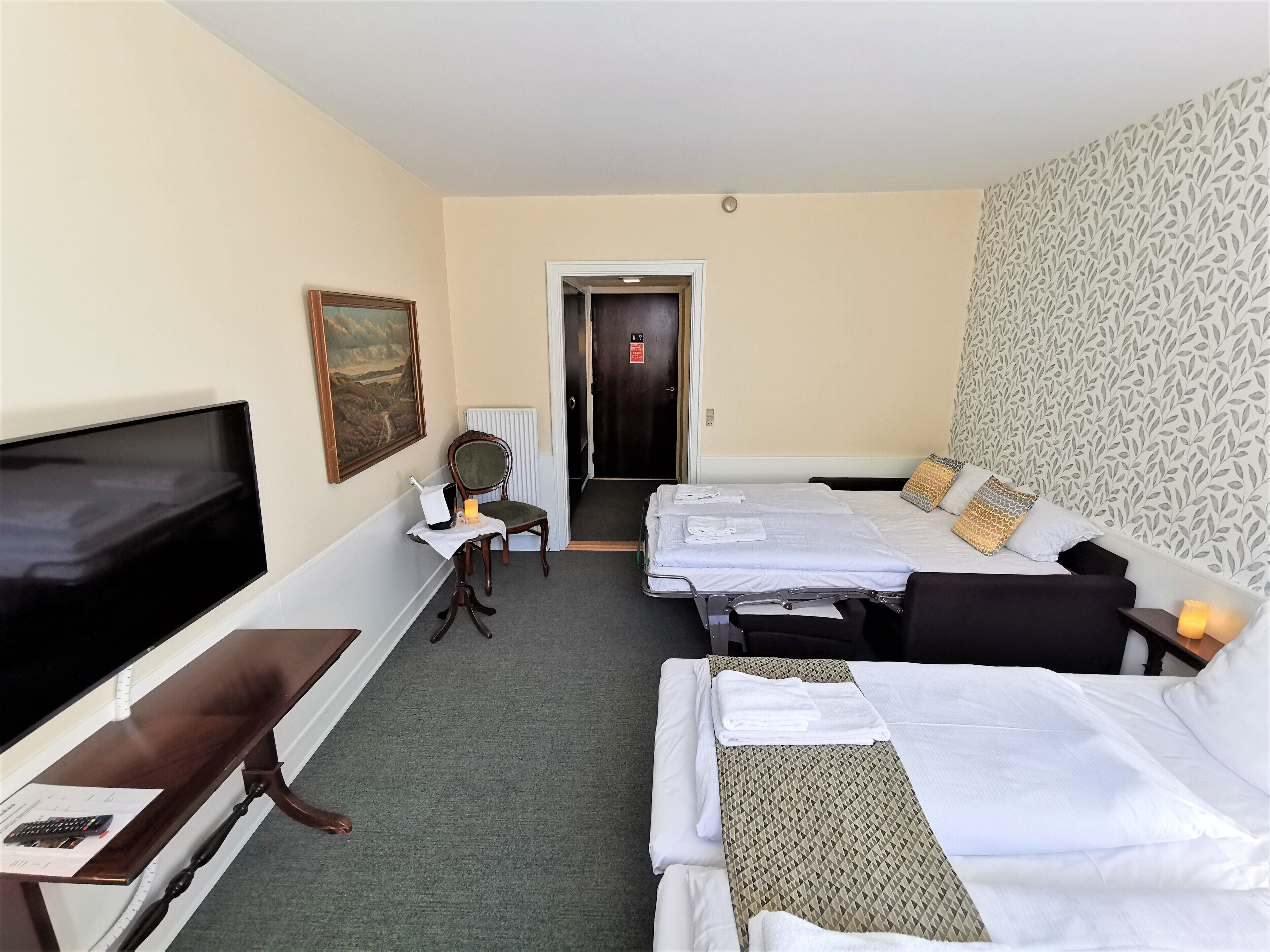 A hotel room with two beds, a TV, a desk with a chair, and a painting on the wall.