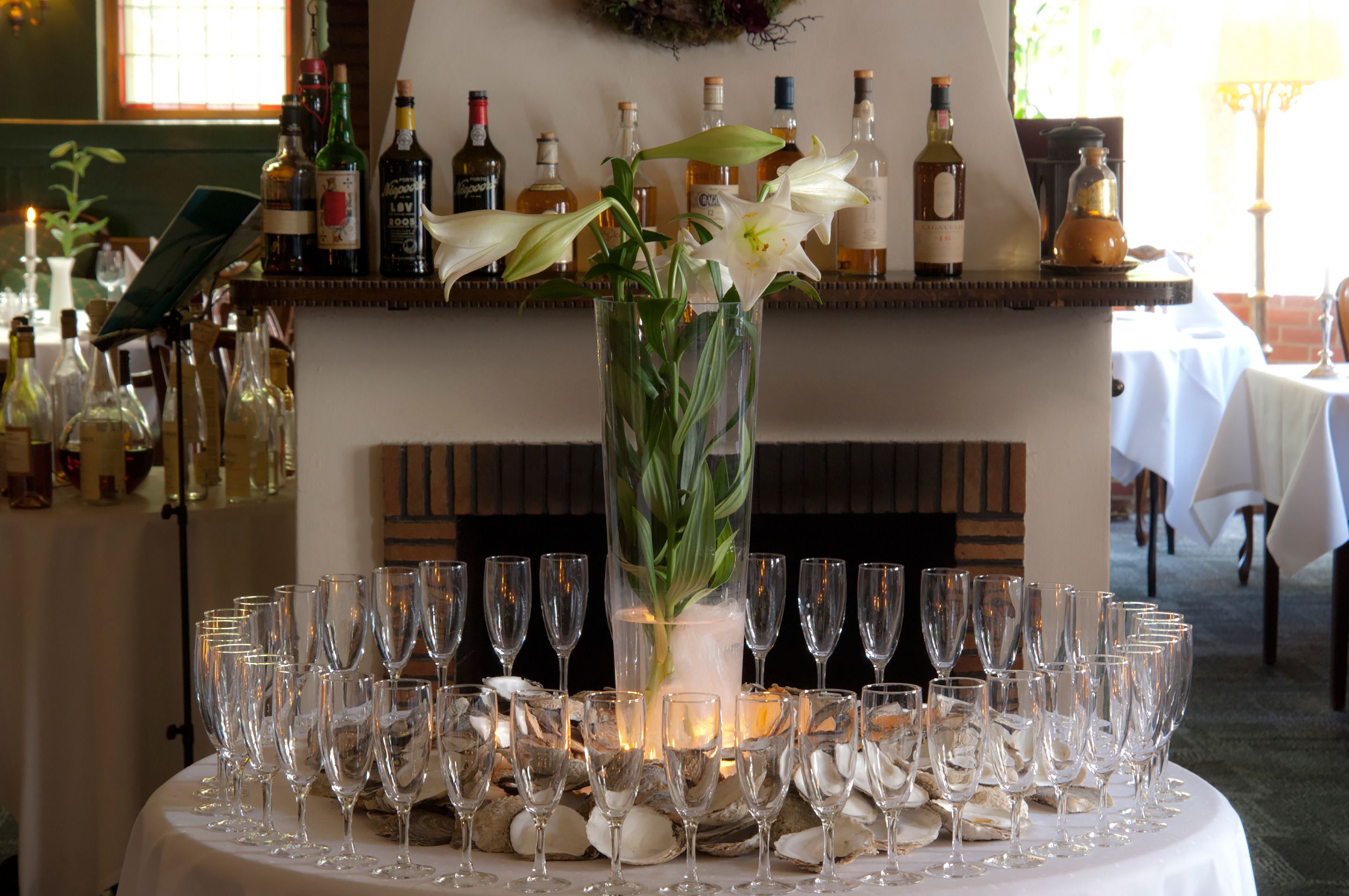 Een tafel gedekt met talloze wijnglazen, gerangschikt rond een middelpunt van een hoge vaas met bloemen.
