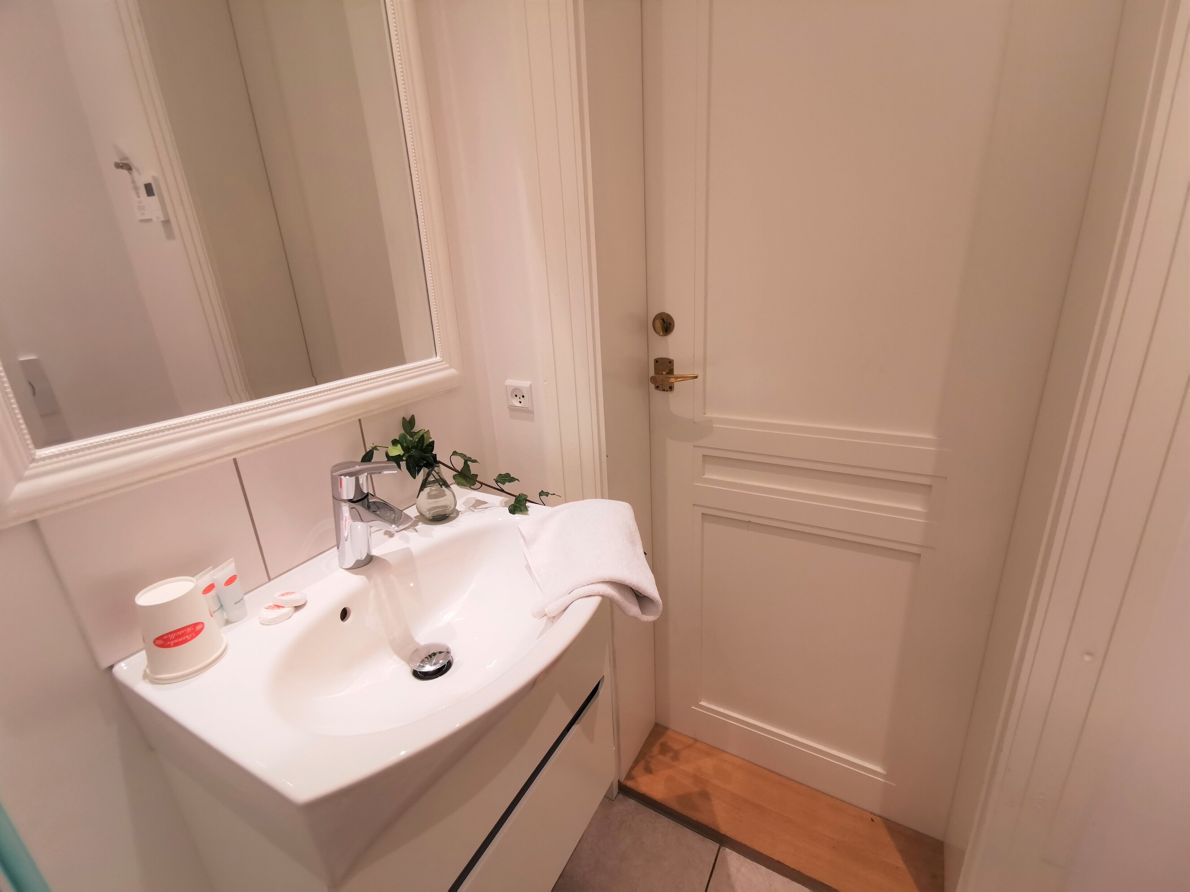 Une salle de bain avec un lavabo blanc, un miroir, une serviette et une petite plante.