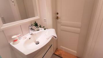 Une salle de bain avec un lavabo blanc, un miroir, une serviette et une petite plante.