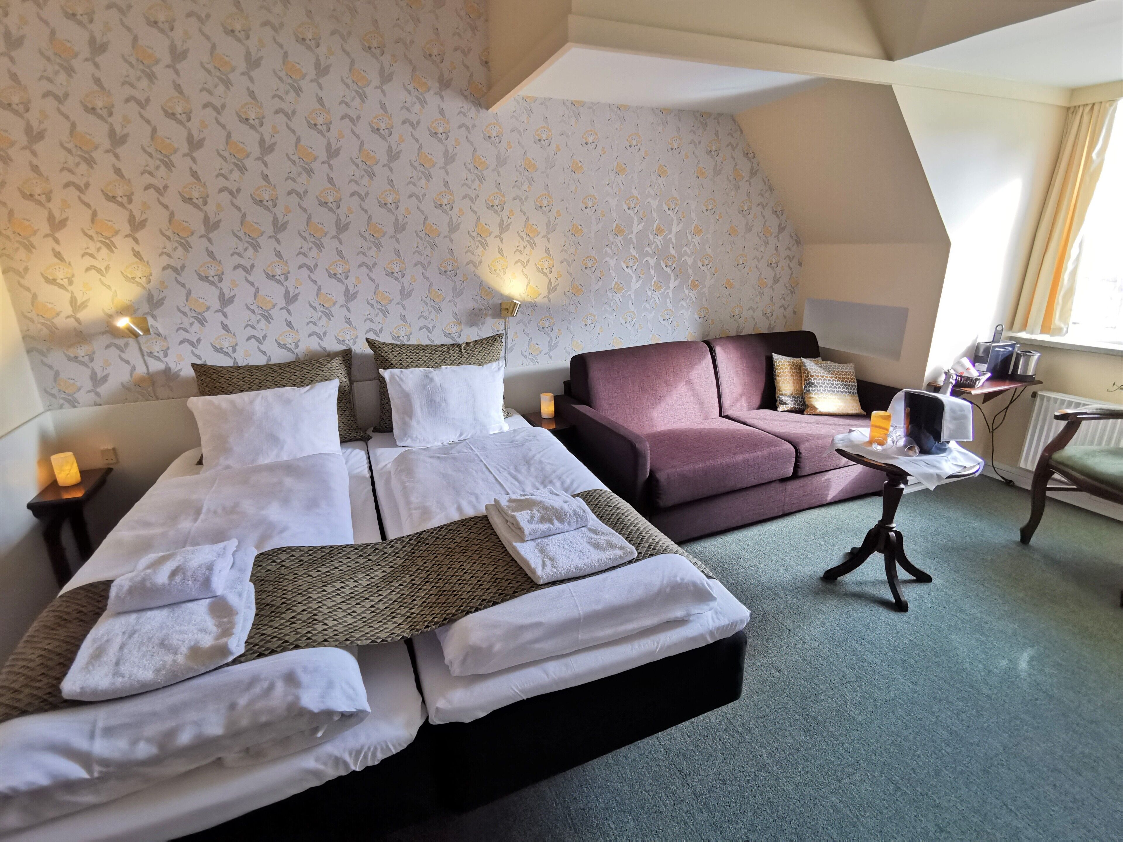 A hotel room with two beds, a sofa, a small table, and a lamp.