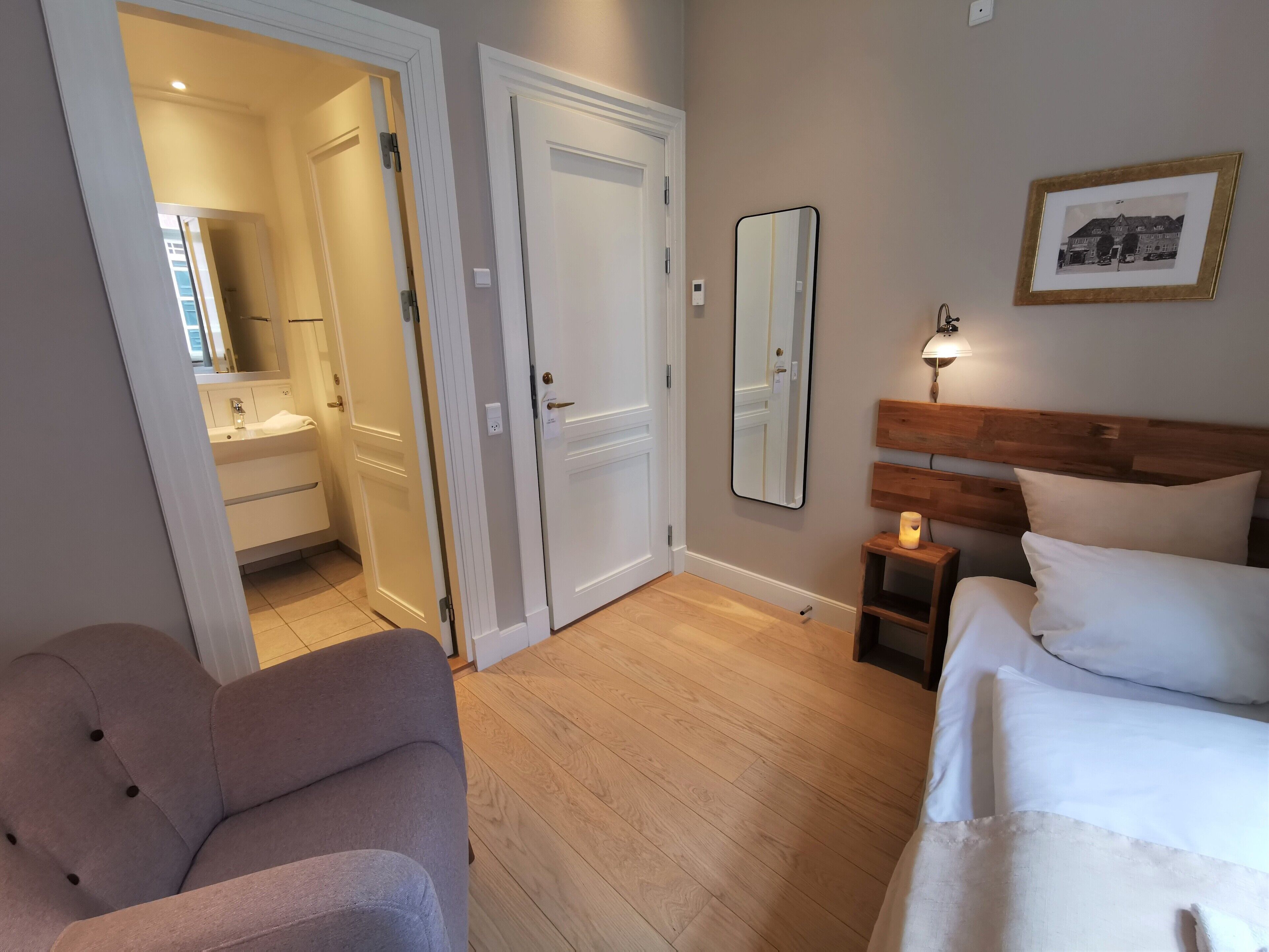 A hotel room with a bed, a bedside table with a lamp, a mirror, and a framed picture on the wall.