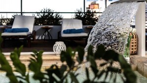A rooftop terrace with a water feature, lounge chairs, and a decorative lantern. - Coral Hotel Athens (Palaio Faliro)