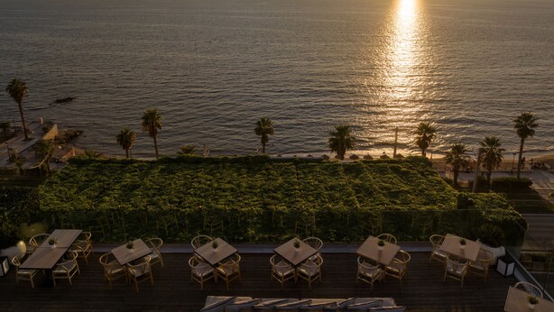A sunset view from a terrace with tables and chairs, overlooking a calm sea and distant mountains. - Coral Hotel Athens (Palaio Faliro)
