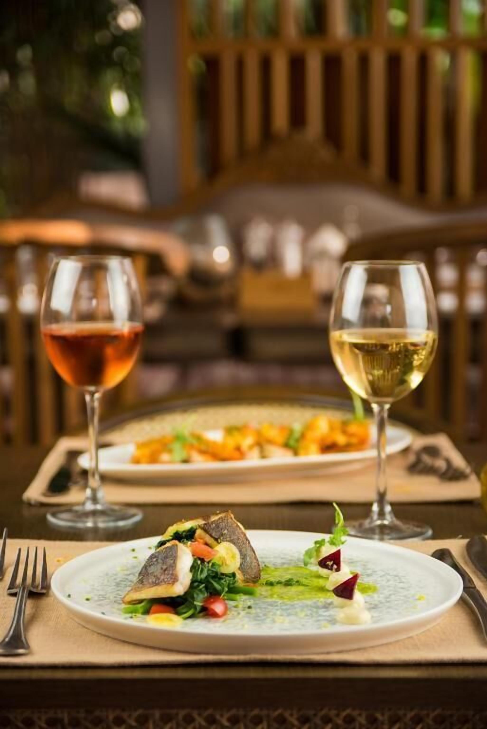 A dining table with two plates of food and two glasses of wine.
