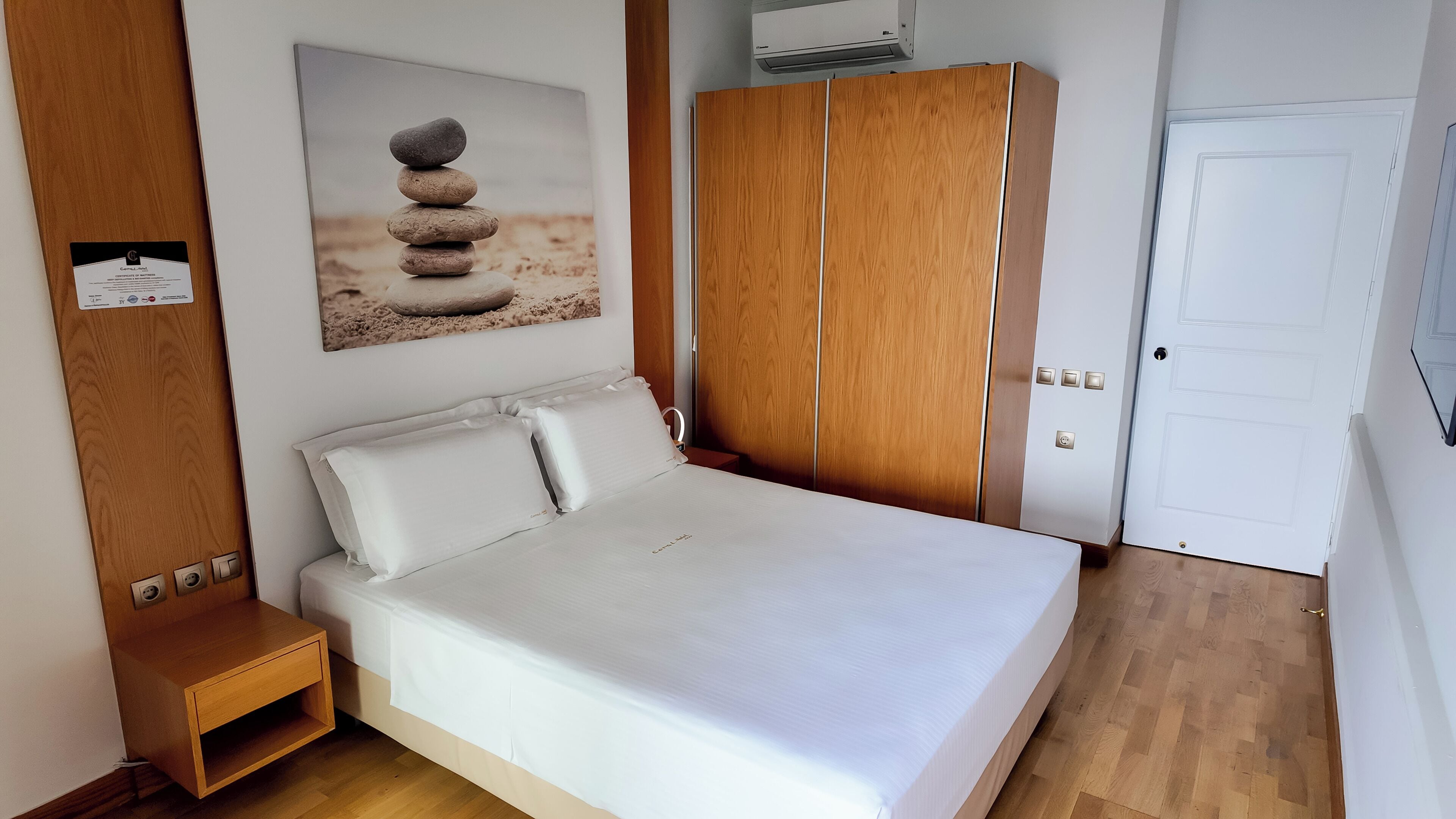 A bedroom with a bed, wooden wardrobe, and a painting of stacked stones.