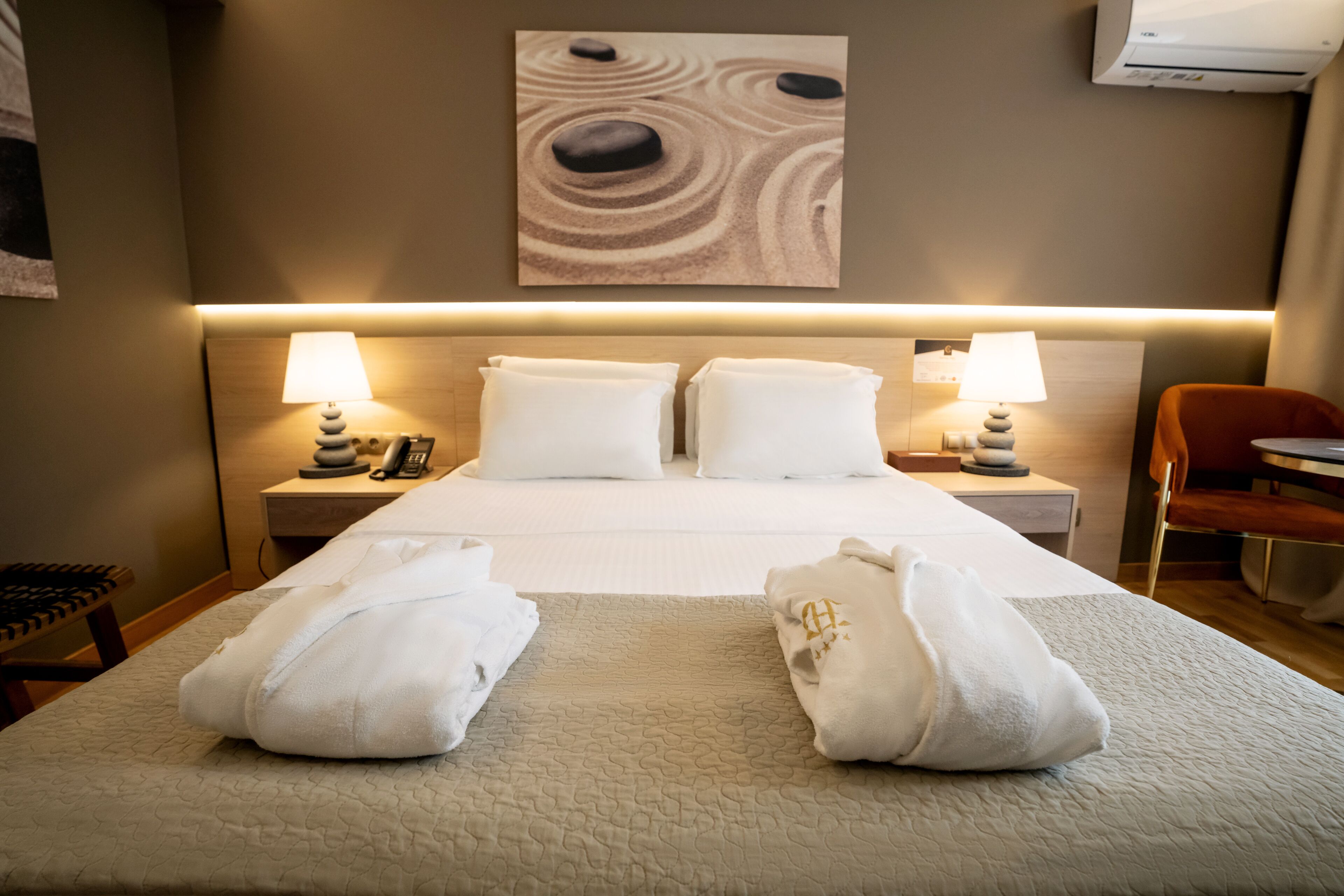 Une chambre d’hôtel avec un lit bien fait, deux lampes de chevet, un tableau décoratif au mur et une chaise.