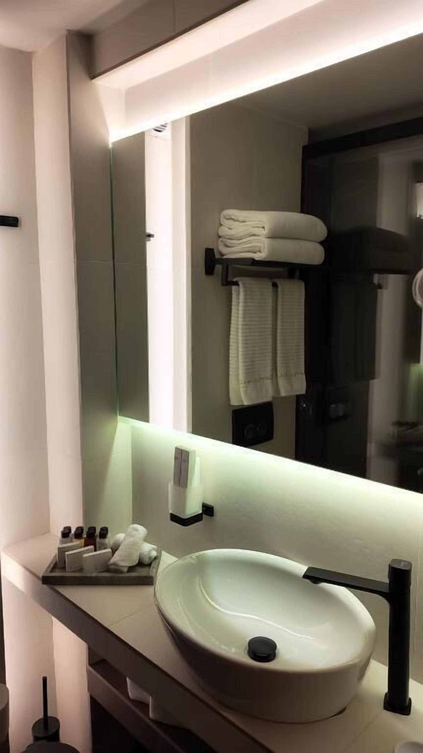 A modern bathroom with a large mirror, a round sink, and neatly folded towels on a rack.