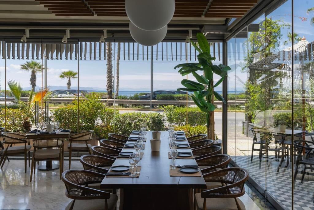 A dining area with a long table set for a meal, surrounded by wicker chairs, with a view of the outdoors.