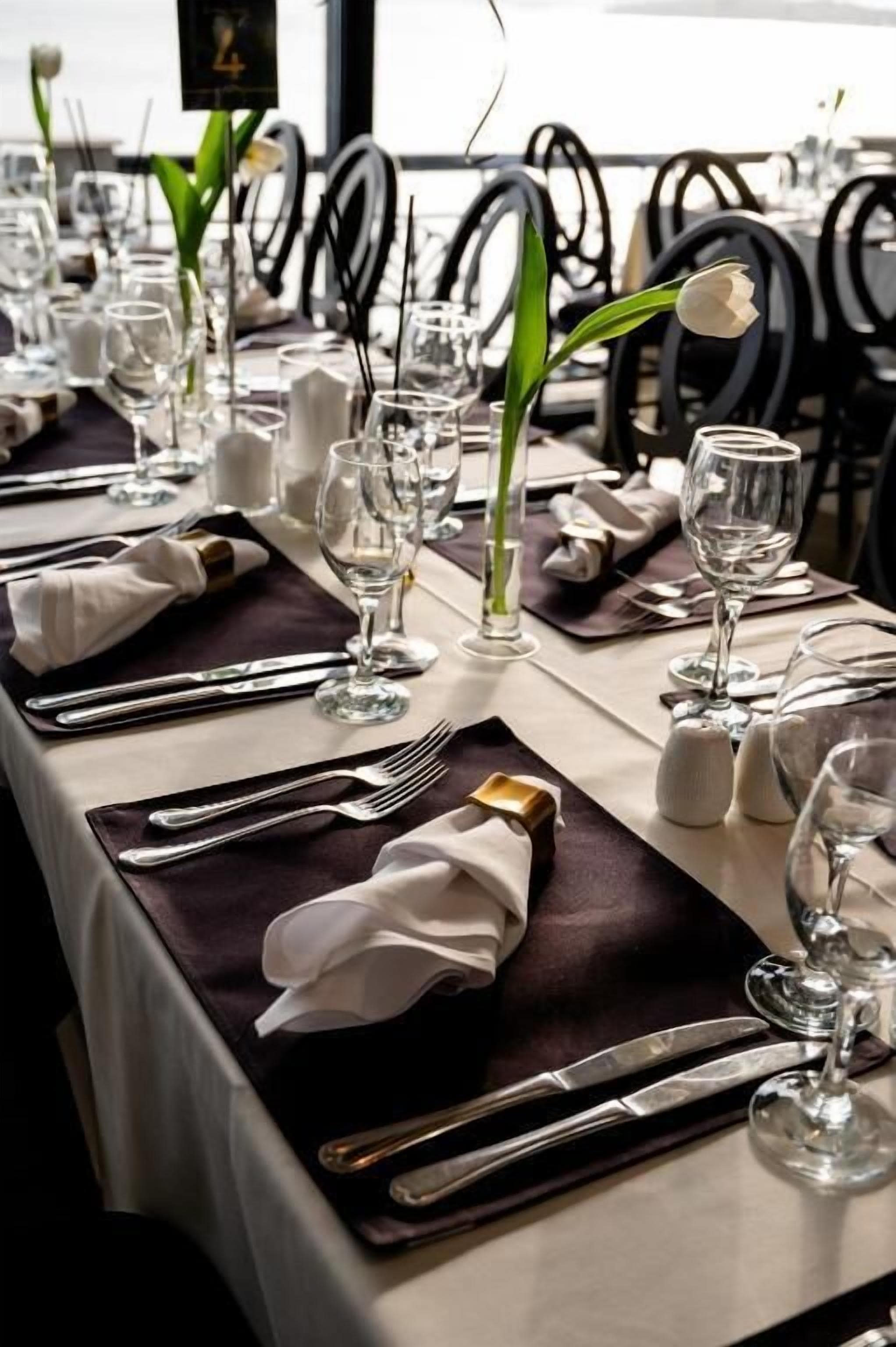 A neatly set dining table with a white tablecloth, black napkins, and silverware.