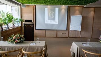 Un salón de conferencias con una pantalla para presentaciones, una pizarra y mesas con sillas.