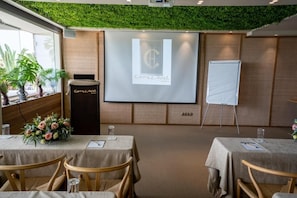 Uma sala de conferências com tela de projeção, quadro branco e mesas com cadeiras.