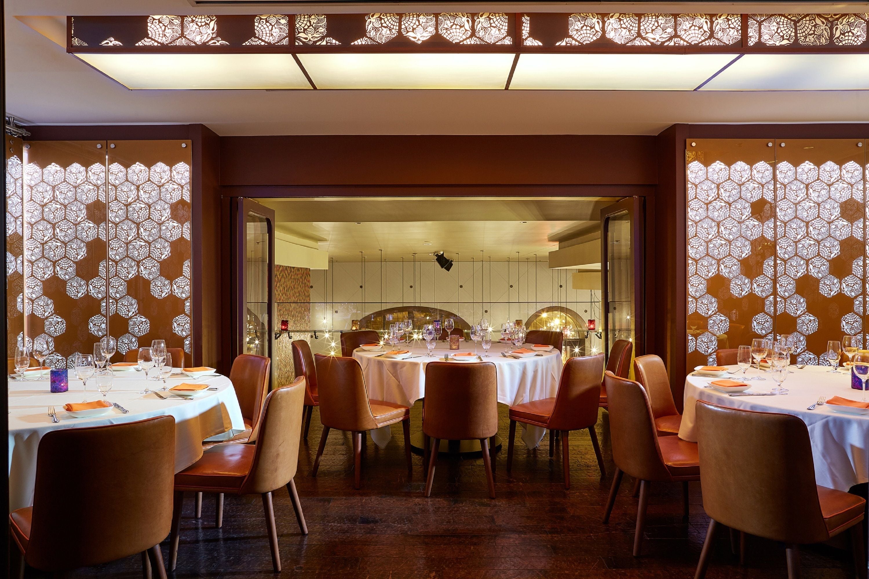A dining area with round tables set for multiple guests, featuring a patterned backdrop and warm lighting.