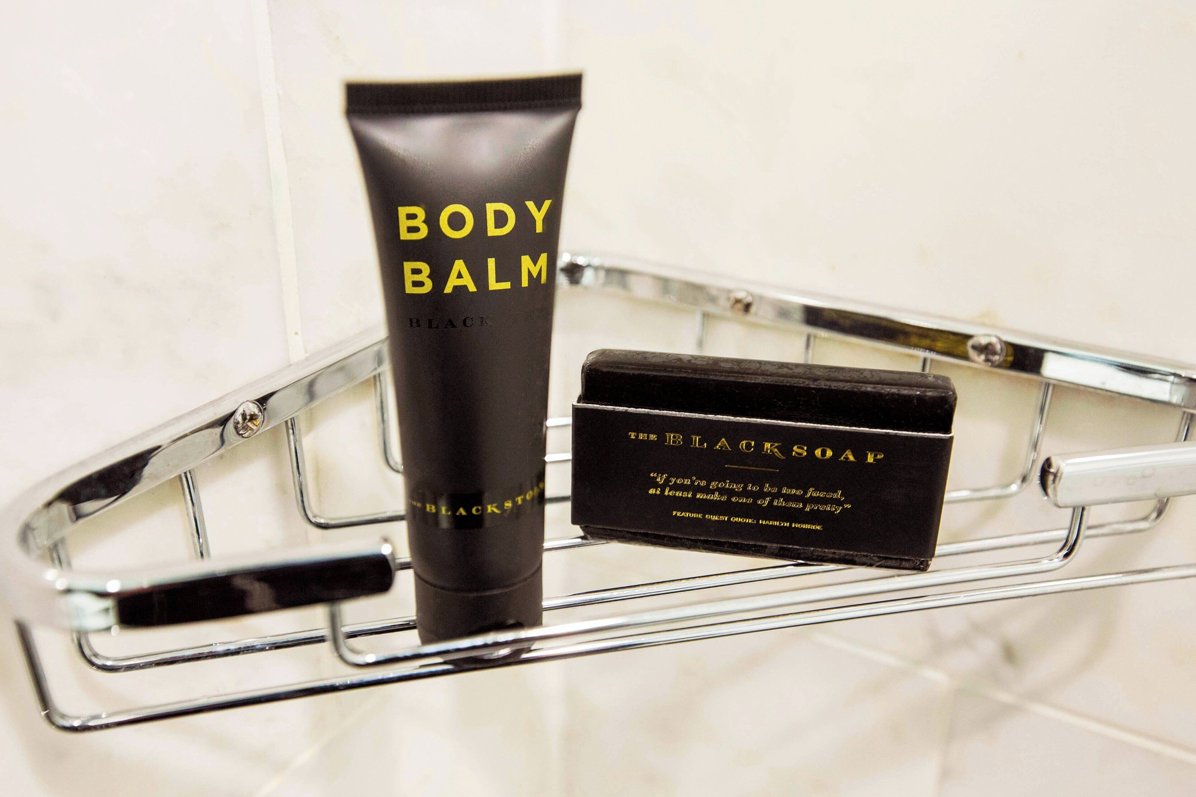 Een badkamerplank met een tube body balm en een zwarte zeep.