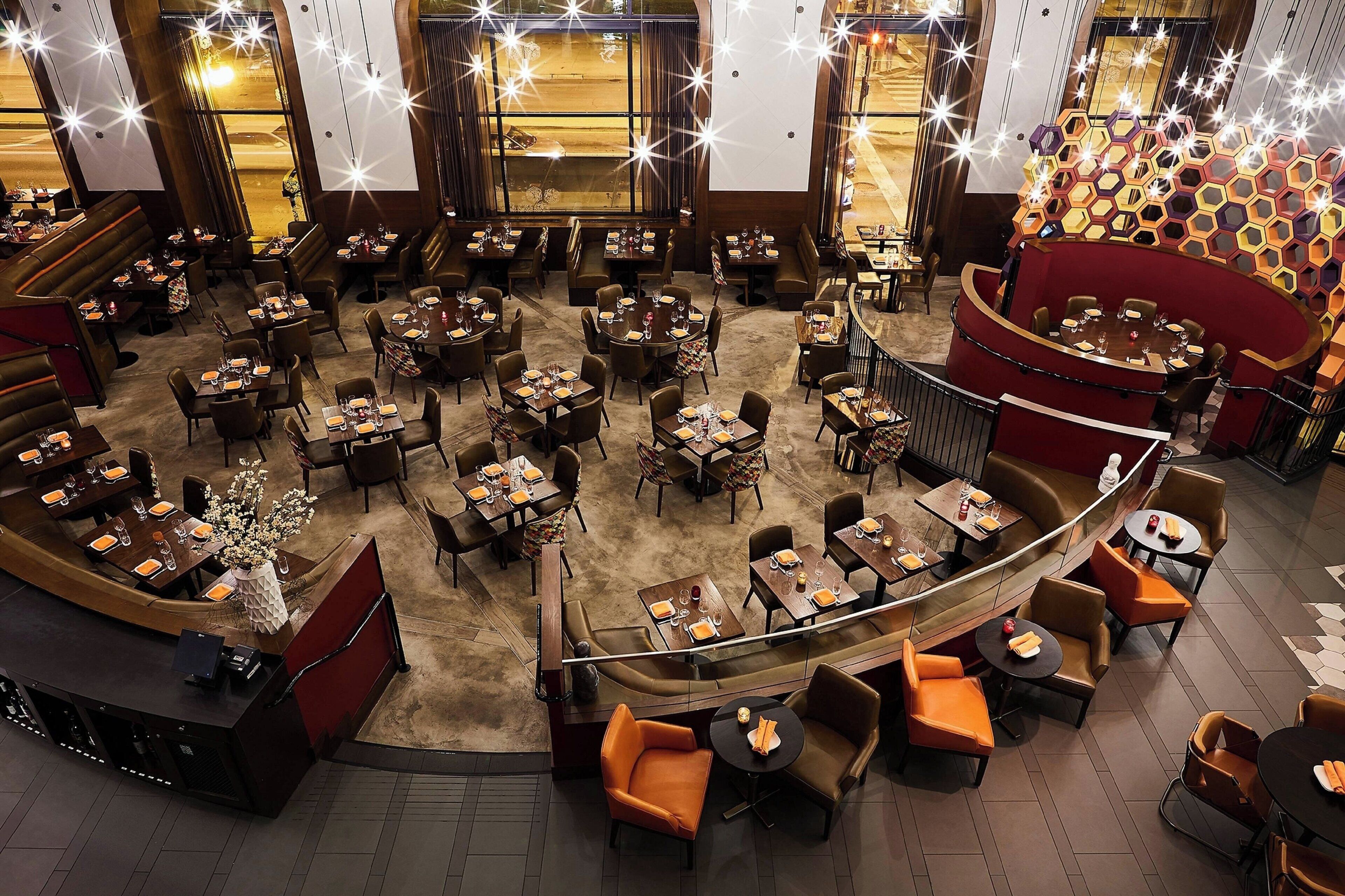 Um restaurante amplo com várias áreas de refeições, incluindo cabines e mesas, e uma área central com parede de destaque vermelha.